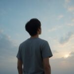 静かな場所でひとり空を見上げる若い人物の後ろ姿。柔らかな青空と薄い雲。希望と内省がゆっくり満ちる雰囲気の横長写真。 Back view of a young person quietly looking up at a soft blue sky with gentle clouds. Calm mood and a sense of quiet hope.